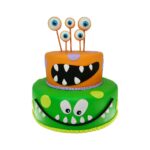Bolo cenográfico de dois andares decorado com o tema monstrinhos. O primeiro andar (base) é verde com olhos e um sorriso com dentes, o segundo andar é laranja com uma boa semi aberta preta com dentes brancos, no topo se vê 5 olhos saindo do bolo.